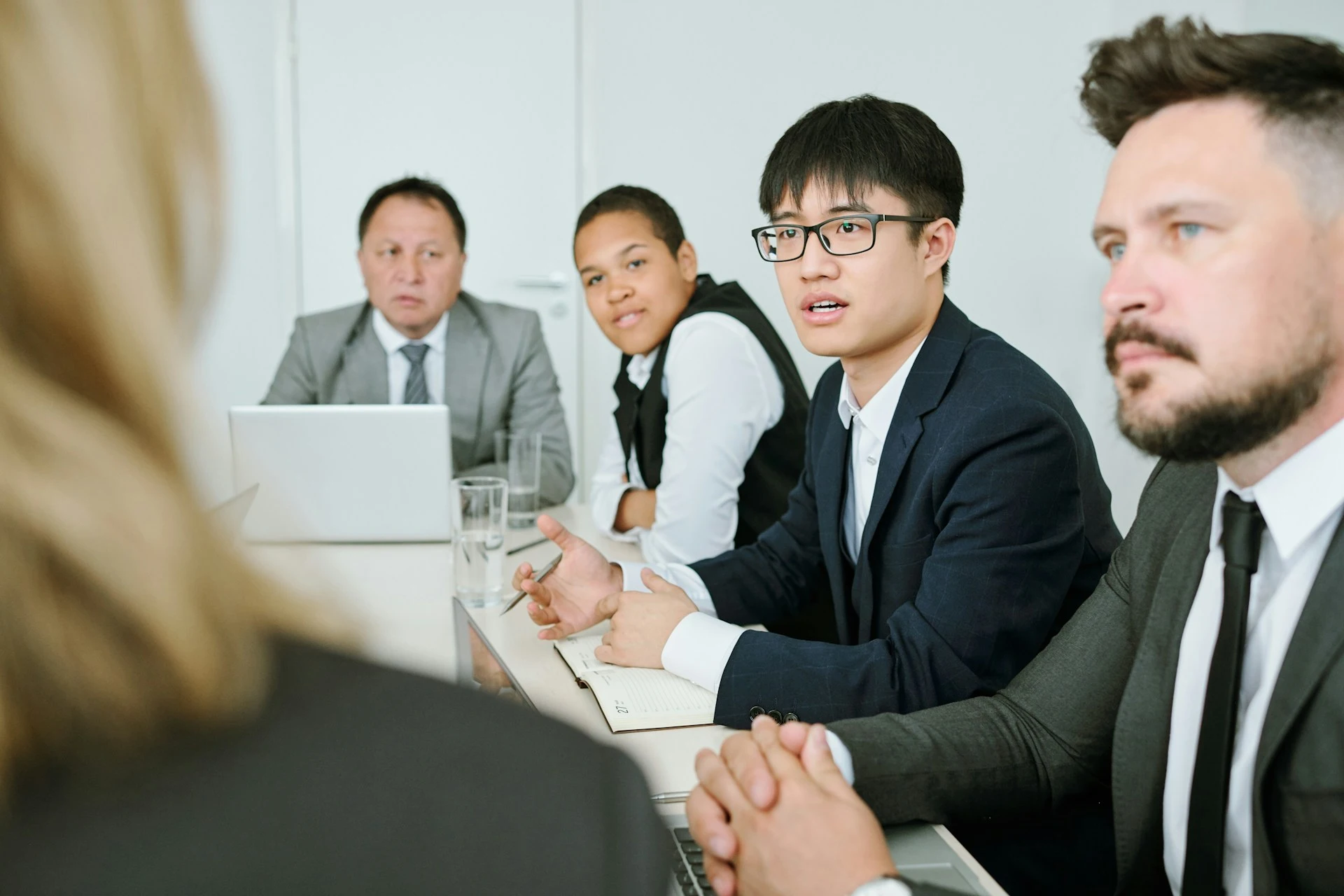 A young businessman with glasses speaking during a professional meeting at a conference table.